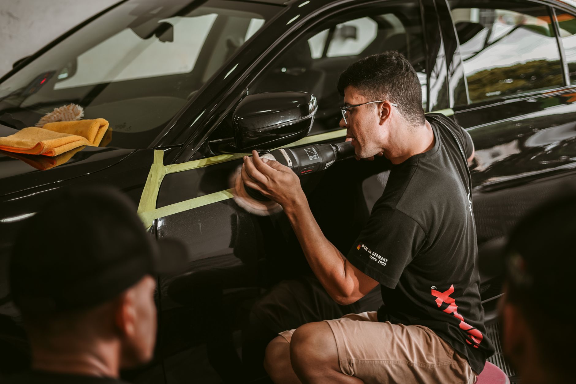 Detailer using a masked-off machine polisher for careful paint correction on a car panel